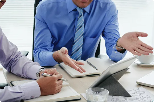 Two professionals in dress shirts engaged in discussion over documents and a tablet.
