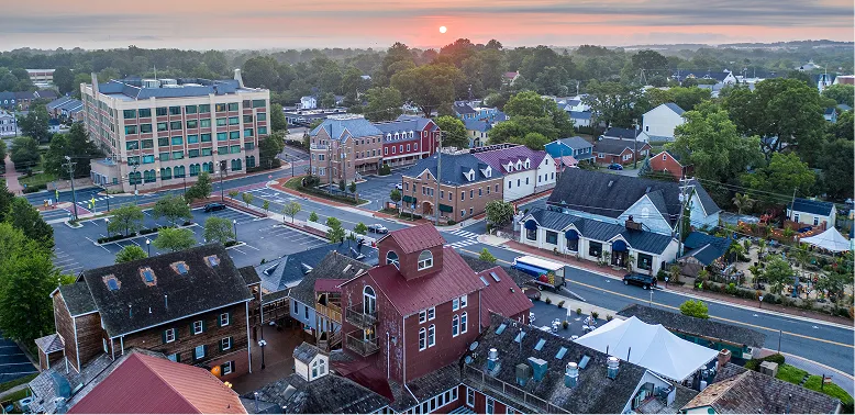 Aerial view of a small town at sunrise with historic and modern buildings, trees, and a clear sky.