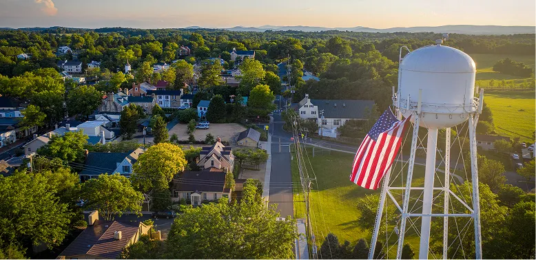Aerial view of a small town with houses and trees, featuring a white water tower displaying a large American flag.