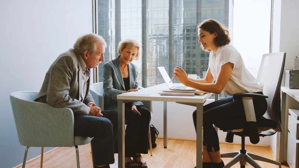 Three people engaged in a professional meeting in a modern office with large windows.