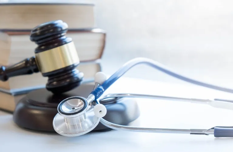 Close-up of a dark wooden gavel, stethoscope, and stacked books on a white surface.