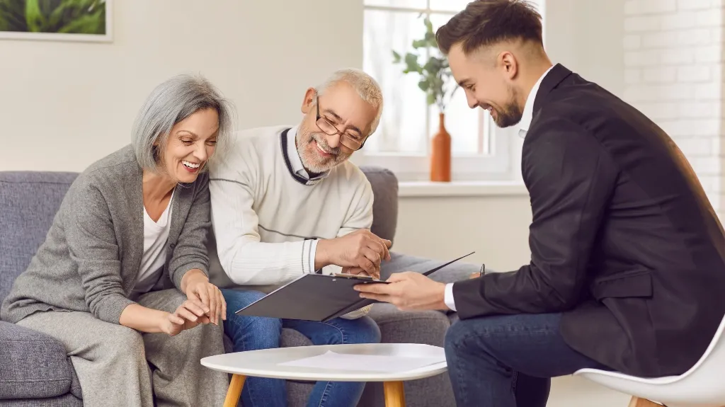 Elderly couple reviewing documents with a young professional in a modern office setting.