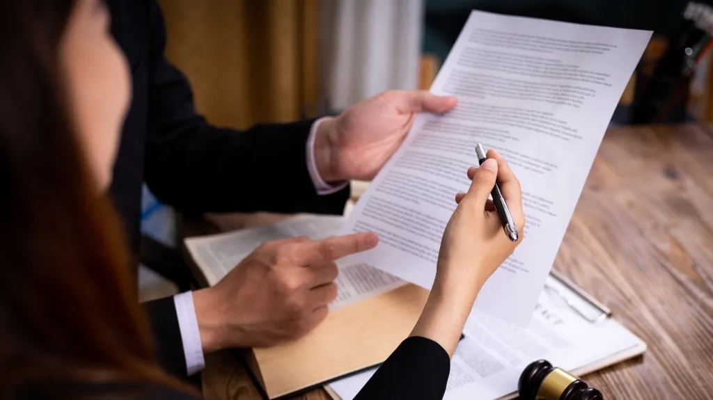 Two professionals reviewing a document with a pen, a gavel and clipboard on wooden table.