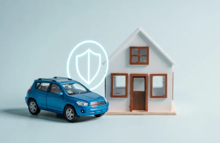 Blue toy SUV and white model house with shield icon representing insurance protection.
